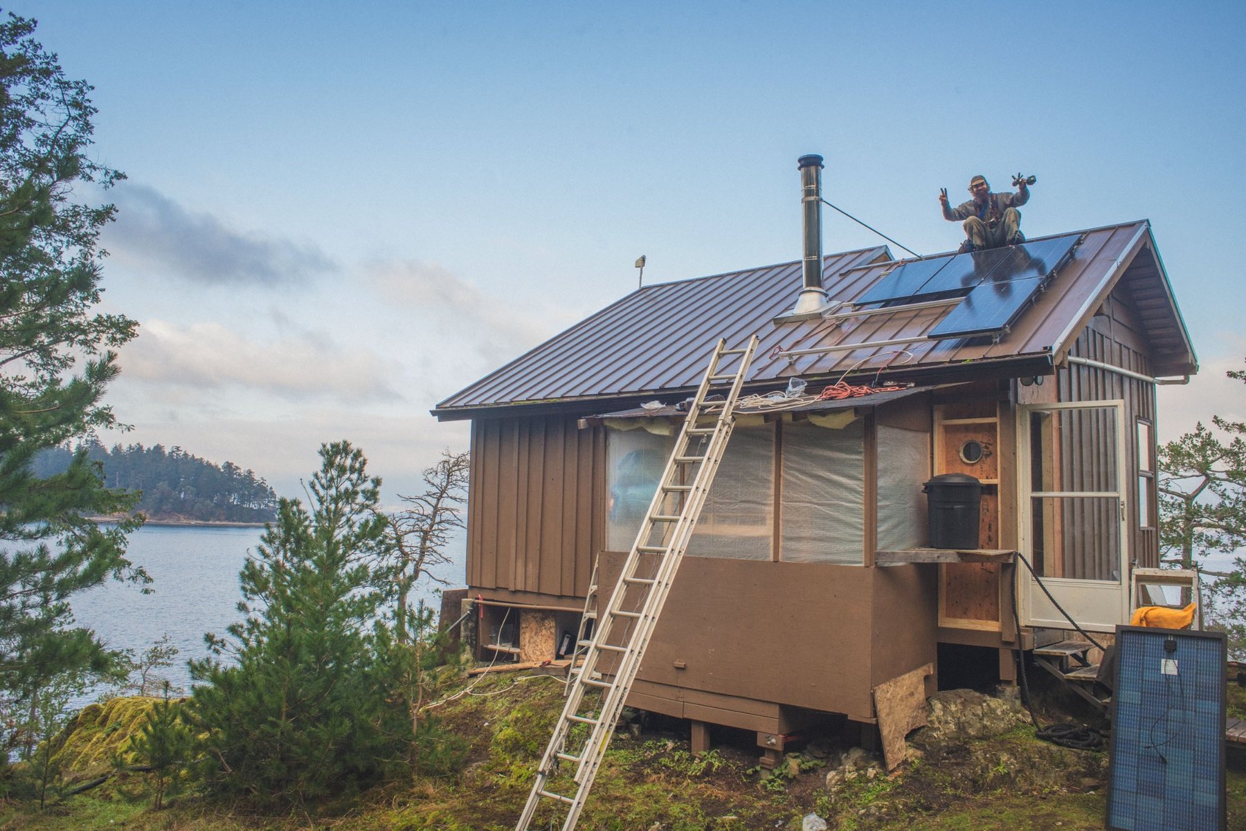 Off-grid cabin with solar panels on a metal roof overlooking the water